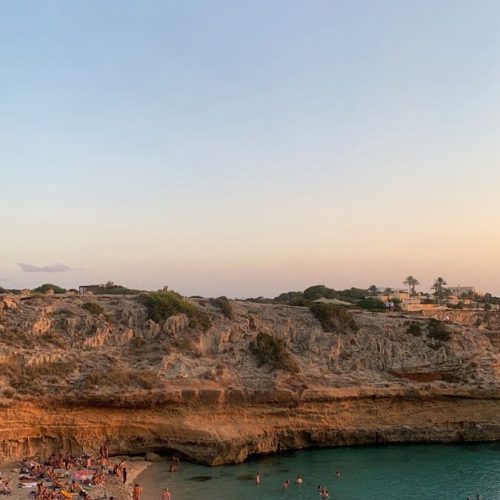 A bay in Ibiza at dusk with people swimming in the Mediterranean waters.
