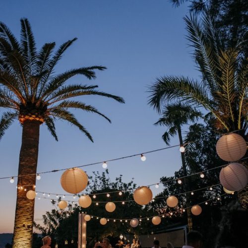An Ibiza beach club at night with fairy lights and palm trees.