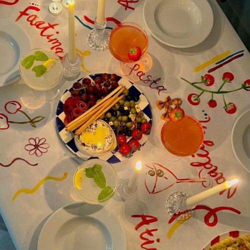 A table set up for a dinner party with a painted table cloth, with guests' names on