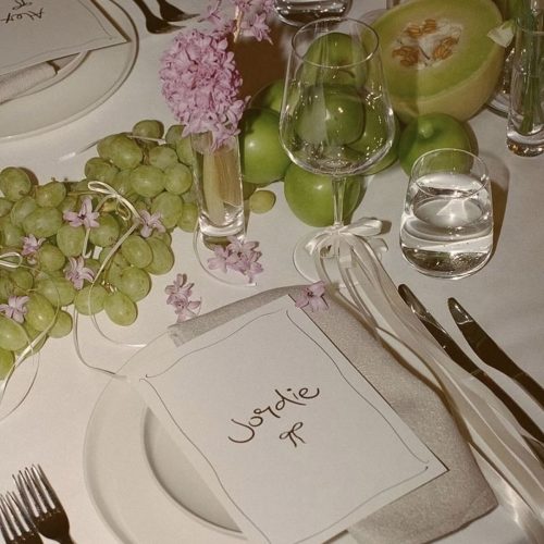 A table set up for a dinner party with a place name on the plate and a table decorated with flowers and grapes