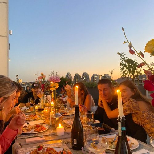 People sat at a long table outside at dusk having a dinner party in the candle light