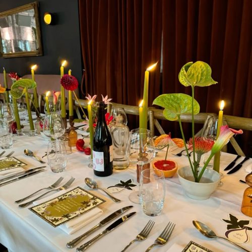 A table set up with unique flowers and plans, wine bottles, and candle sticks