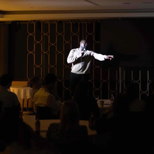 A comedian from Comedy in the Office performing stand-up comedy on stage to a crowd
