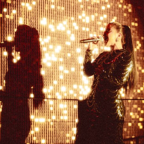 A singer performing at Aretha with a sparkly gold backdrop
