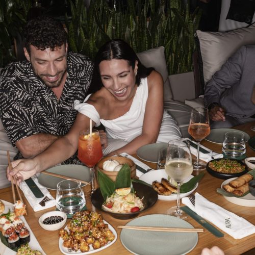 Two people laughing and enjoying sushi and drinks at Aura Skypool
