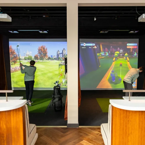 Two booths with people playing in the golf simulations at Pitch