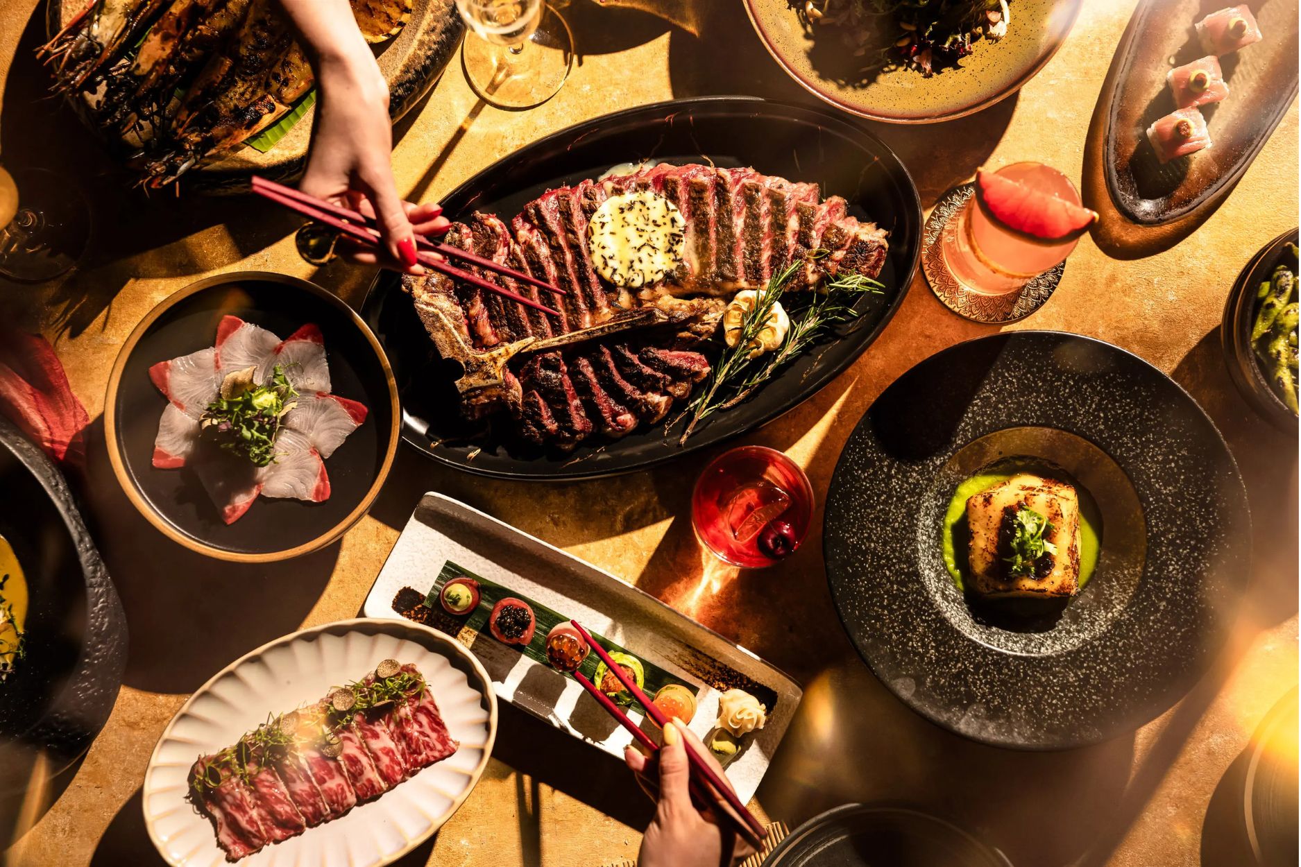 An aerial view of a table of food at CÉ LA VI, including a sharing steak and cocktails