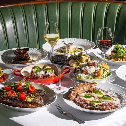 A table of food served at Carbone, including steak, meetballs, and glasses of wine
