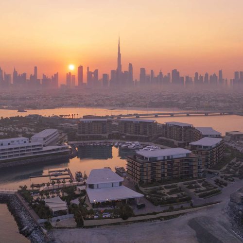 An aerial view of the curved Bvlgari Yacht Club, with the sun setting over the Dubai skyline in the background