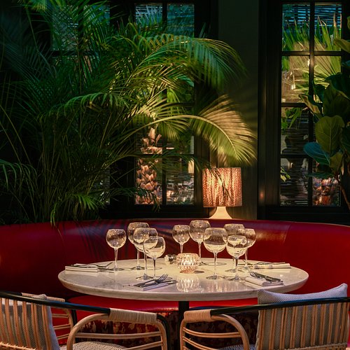 A booth table set up at Eugène Eugène with wine glasses and a large plant nearby