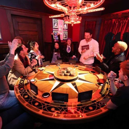 Friends gathered around the round table at The Traitors Experience, working out the challenge and cheering their friends on