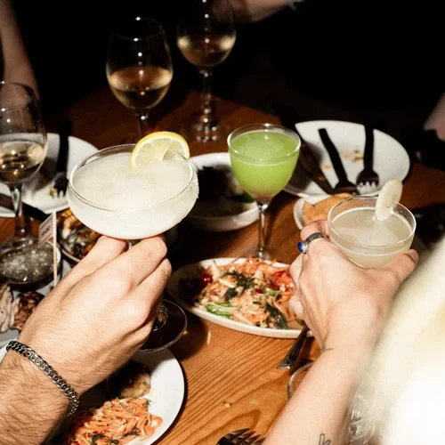 A flash image of friends cheering with margaritas and small plates of thai food at Khao Bird