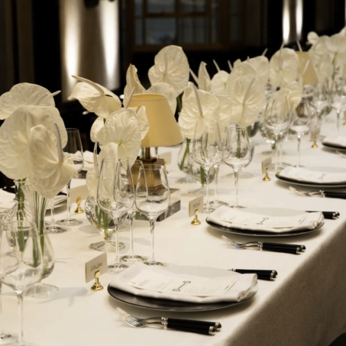 A dinner party laid up on a long table at Landing Canary Wharf, with simple, white decorations lining the table
