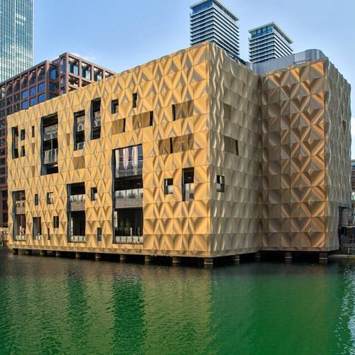 The exterior of Amazing Grace Canary Wharf, which is a gold building on the canal