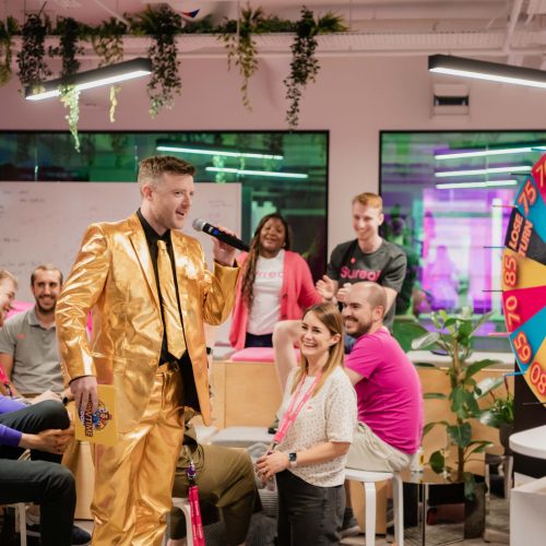 The host from Showtime London introducing a game in the office with a spinning wheel