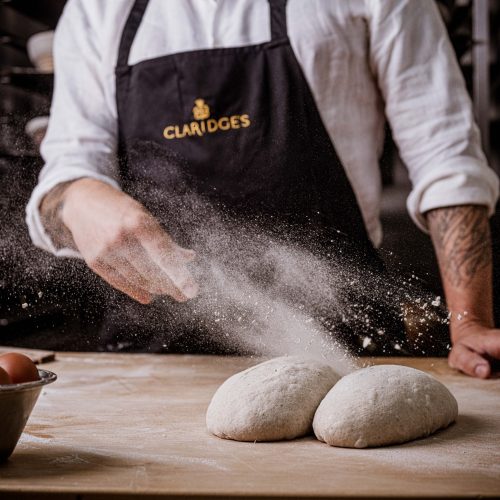 A chef scattering flour on some dough in the kitchen of Claridge's Bakery