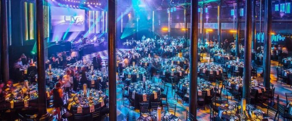A large event venue in London, set up for an awards night and decorated with bright neon lighting