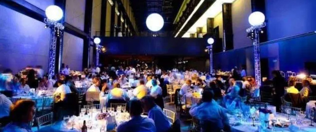 A busy event at the Tate Modern in the Turbine Hall, with round table seating and blue lighting