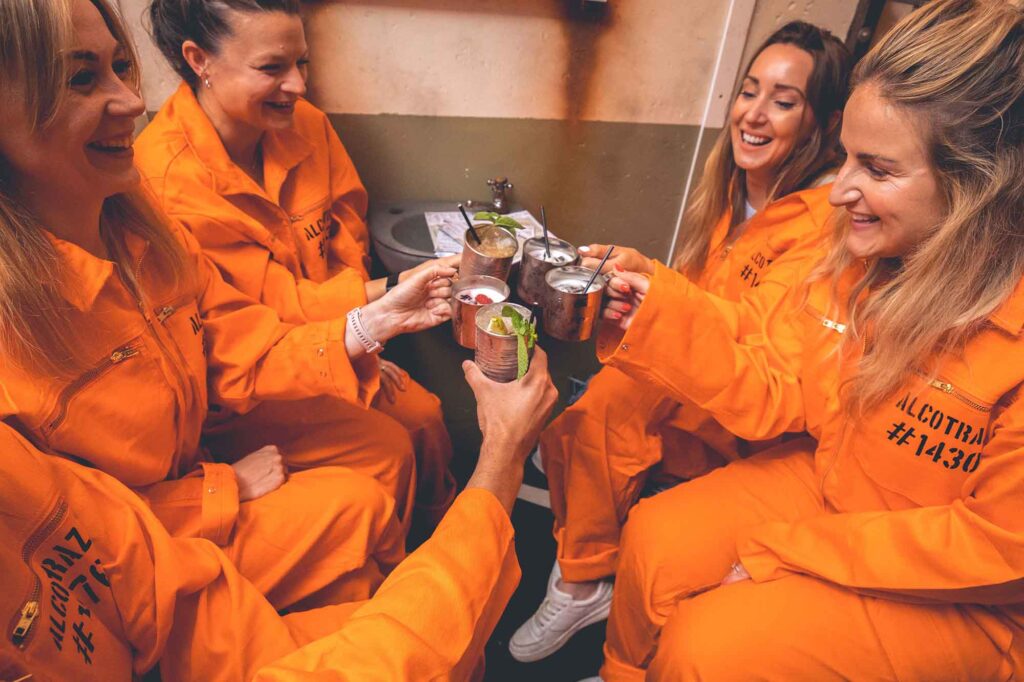 A group cheering drinks wearing orange jumpsuits at the immersive Alcotraz experience in London