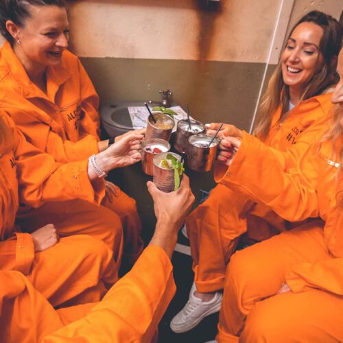 A group cheering drinks wearing orange jumpsuits at the immersive Alcotraz experience in London