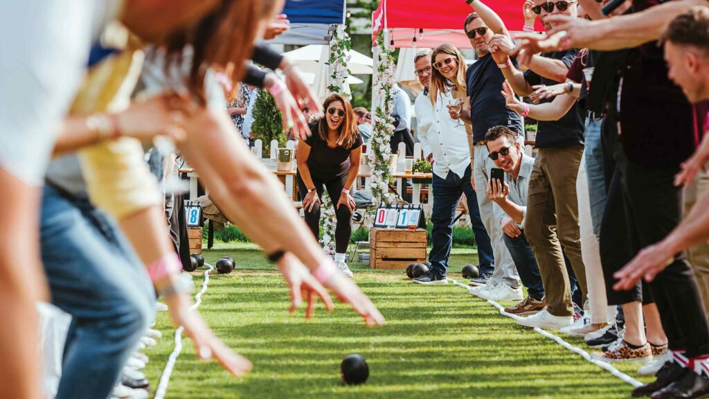 Someone playing bowls at The Bowls Club, while the group cheers from the side of the green