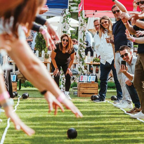 Someone playing bowls at The Bowls Club, while the group cheers from the side of the green