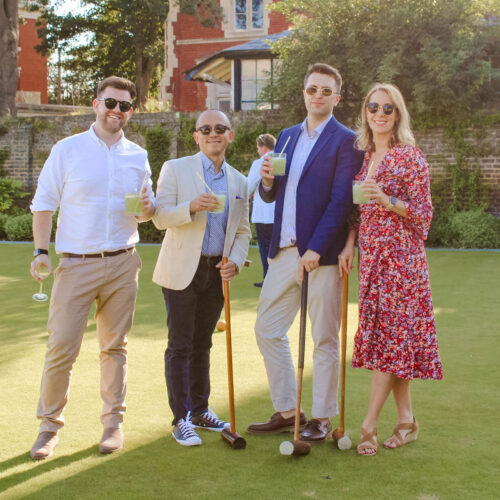 Guests posing for a photo with their cocktails and croquet mallets at Croquet & Cocktails